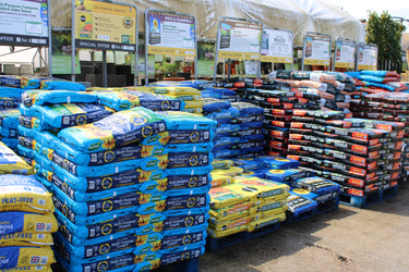 Stacks of garden soil bags in a warehouse setting with promotional signs.